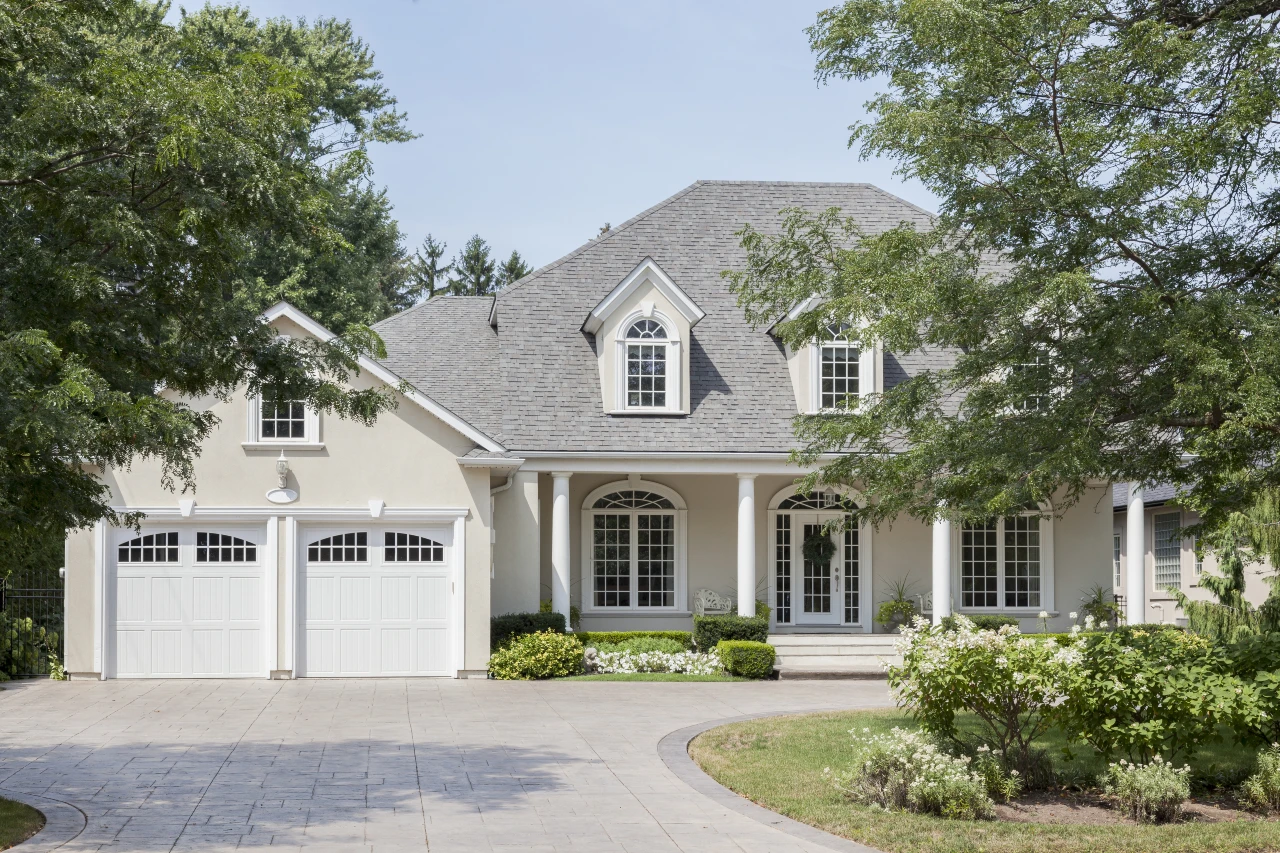 A grey house with trees and white garage doors.